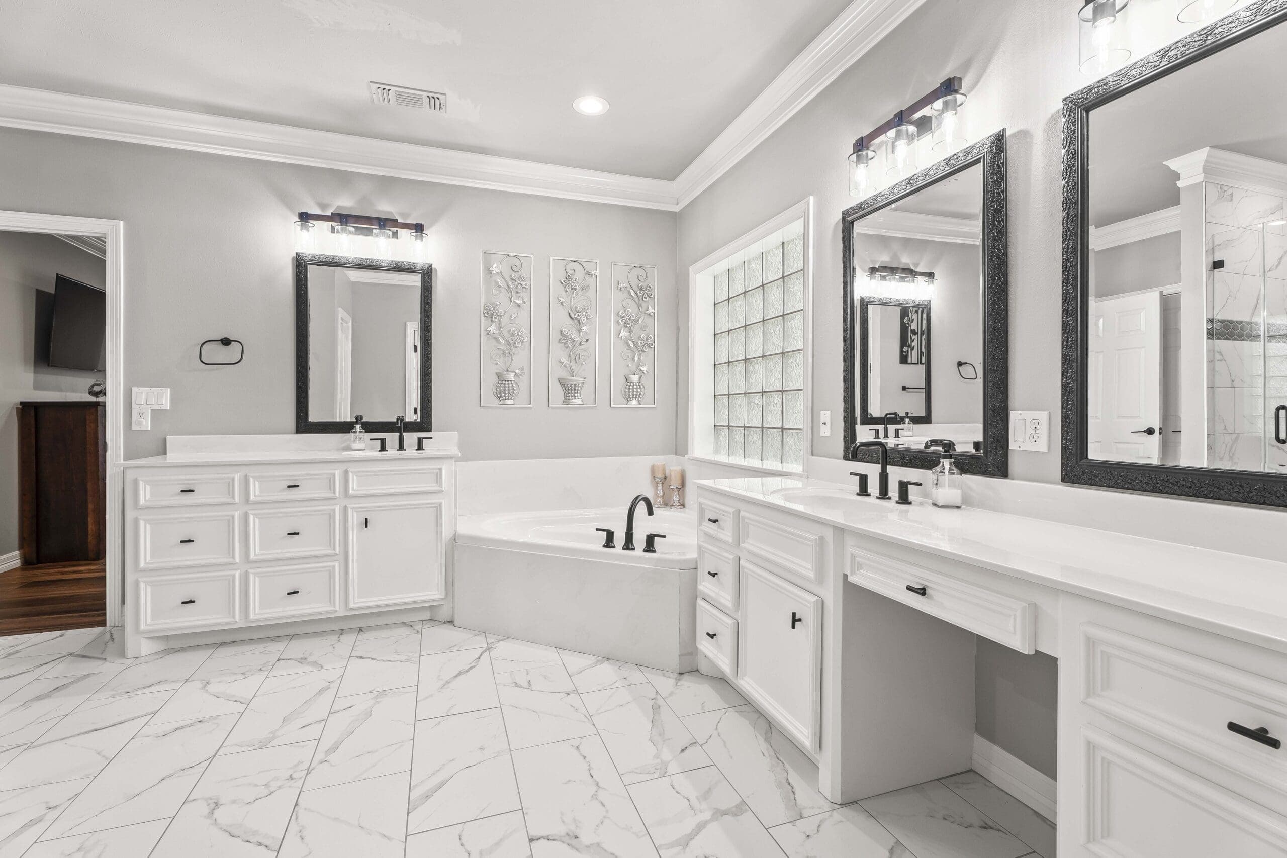 Real estate photography of a primary bathroom with dual vanities, a soaking tub, and marble flooring.