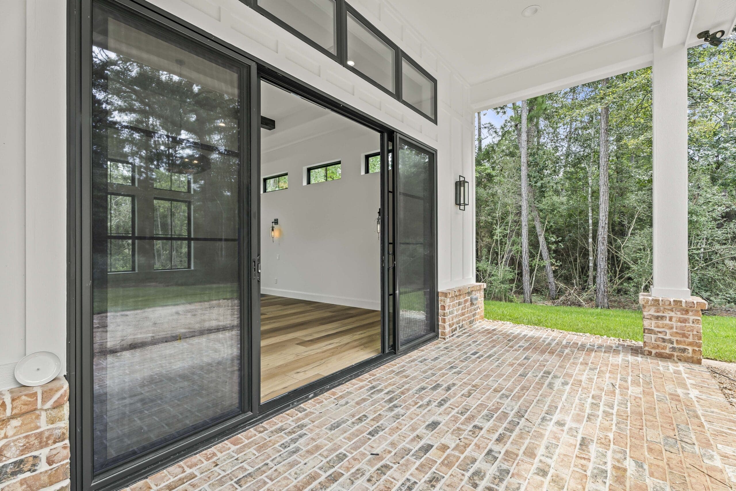 Real estate photography of a covered patio with brick flooring and large sliding glass doors.